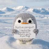 Crocheted penguin holding a sign with motivational text on a snowy background